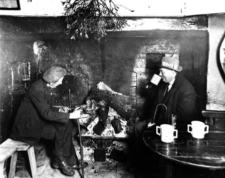 Cider drinkers in a pub at Compton Dundon, c.1930s. Cider was often warmed up in pubs using a special container called a cider shoe. Spirits such as gin and brandy were added to the mixture. A tradition two handled cider mug was often used and can be seen on the table in this photograph.